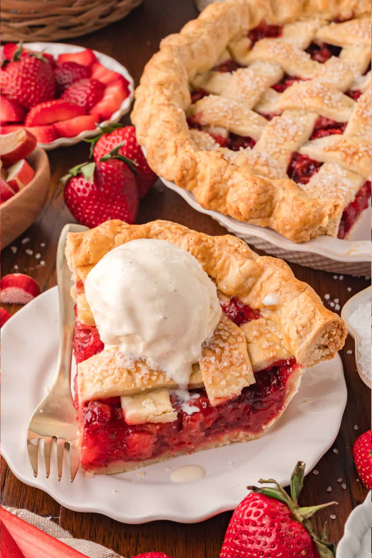 Strawberry Rhubarb pie slice on a plate surrounded by fresh strawberries and slices of rhubarb