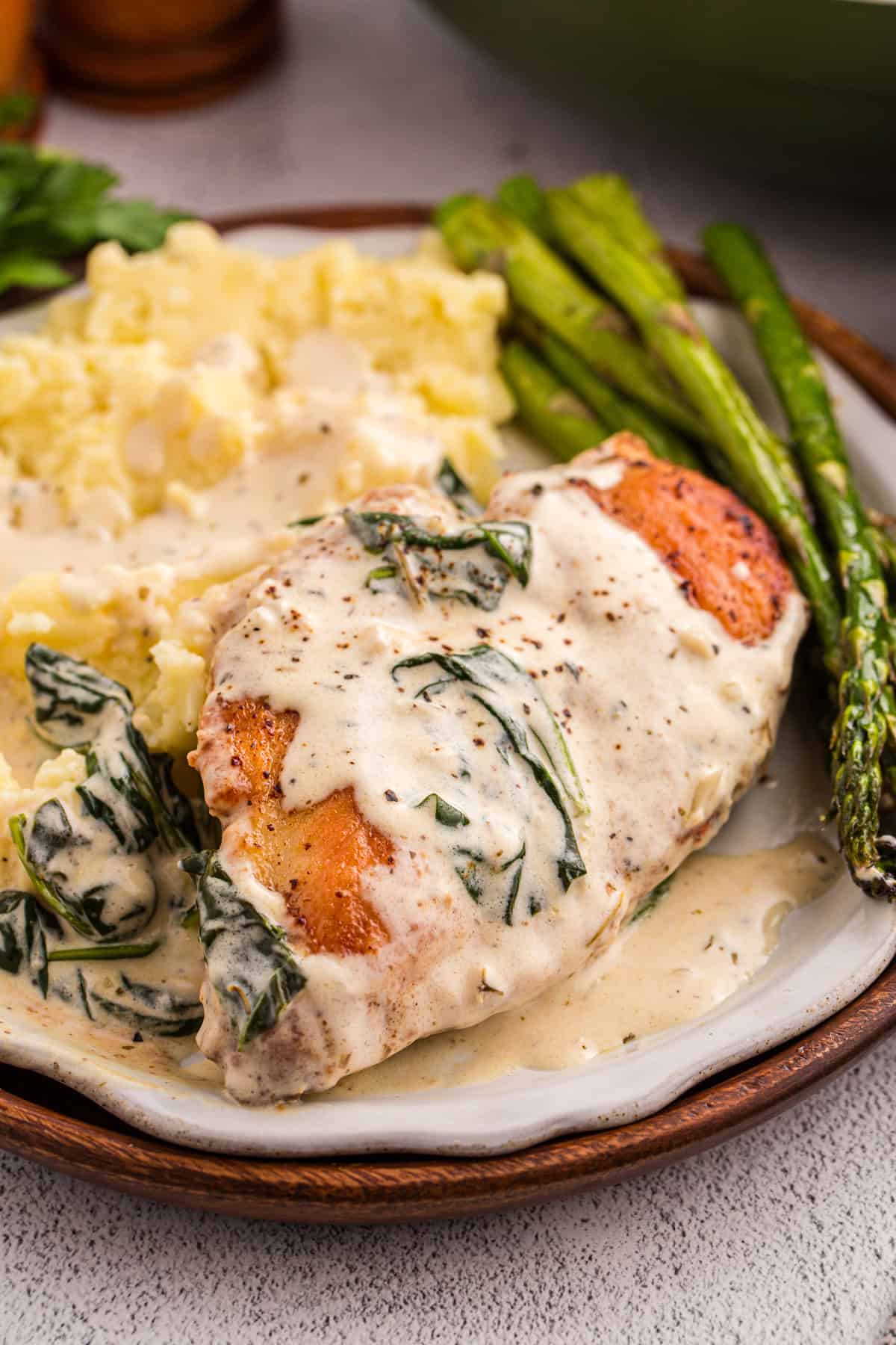 Juicy pan-fried chicken is coated in a creamy, garlicky white wine sauce with spinach and freshly grated parmesan in this Chicken Florentine. A plate of chicken florentine with mashed potatoes and asparagus