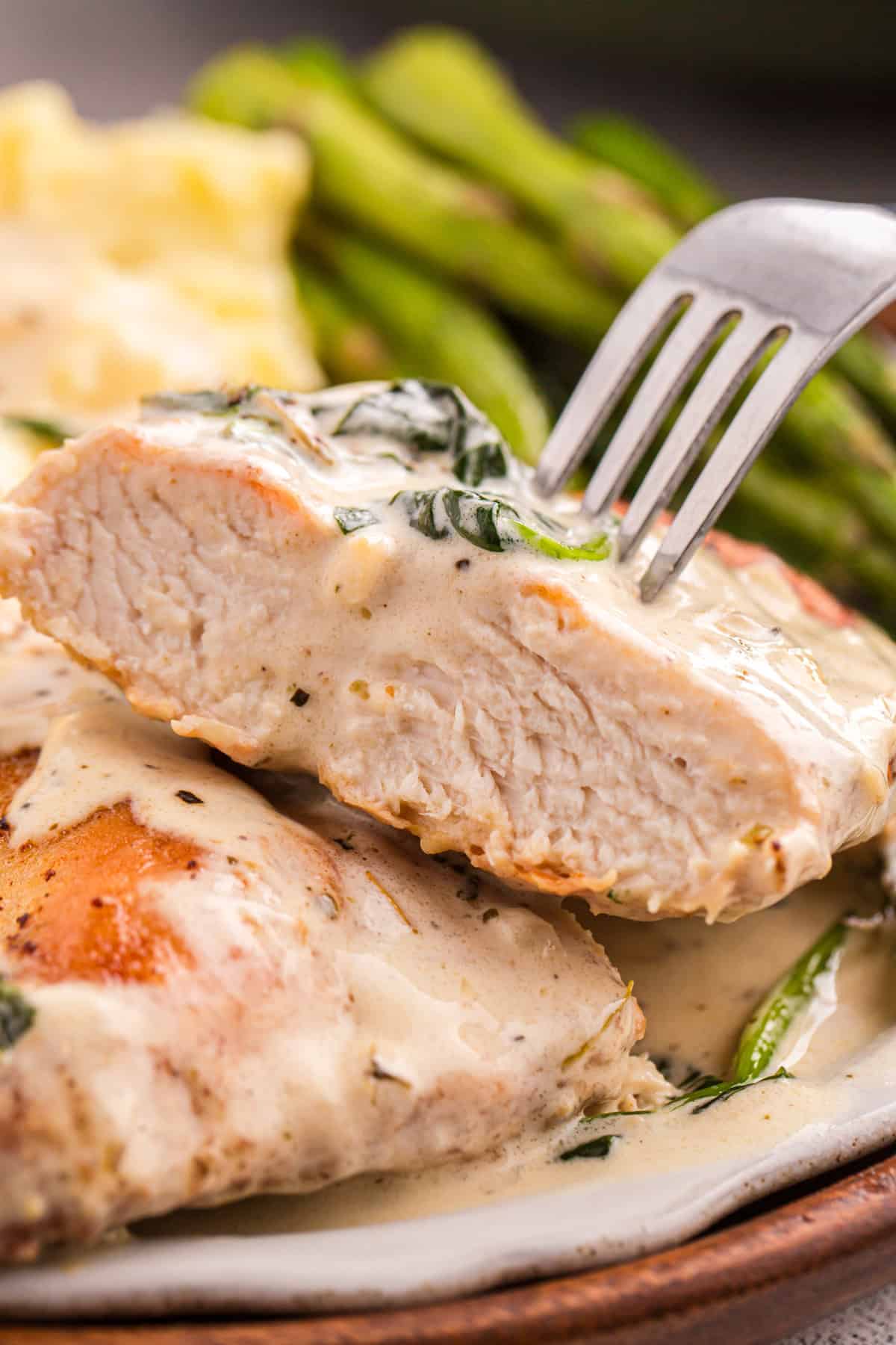 Juicy pan-fried chicken is coated in a creamy, garlicky white wine sauce with spinach and freshly grated parmesan in this Chicken Florentine. A fork in a piece of chicken florentine