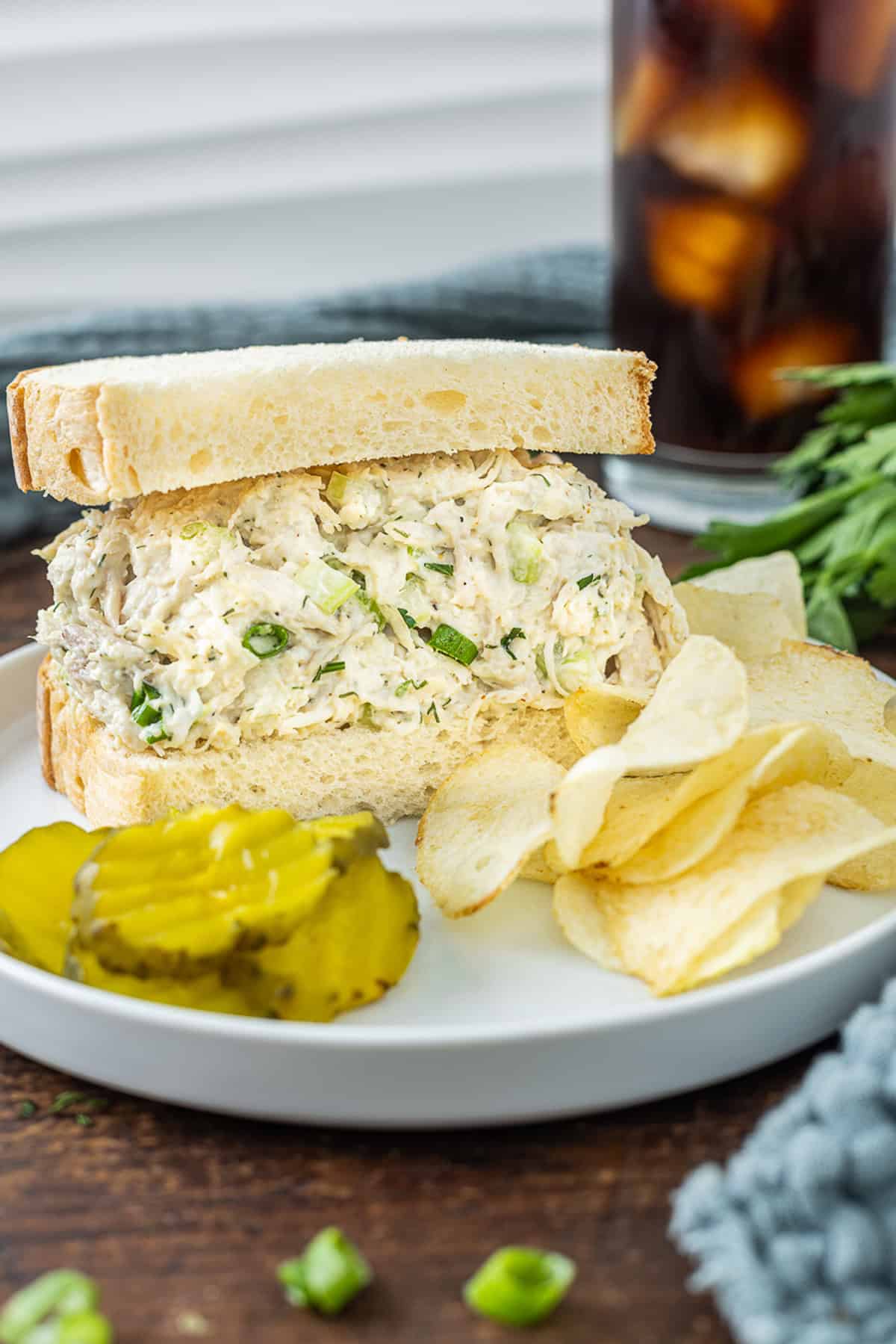 This Classic Chicken Salad Recipe is a simple, no-frills lunch made with shredded chicken, celery, & green onions tossed with mayo and dill. A chicken salad sandwich on a plate with chips and pickles