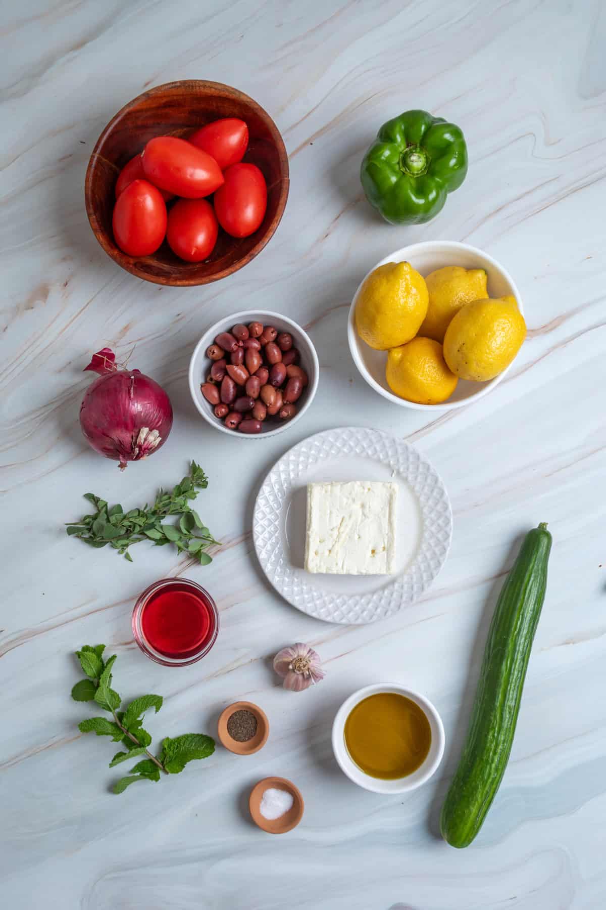 This traditional Greek Salad is made with simple ingredients & bold flavors, like fresh veggies, Kalamata olives, and feta cheese. Overhead view of ingredients needed to make Greek salad