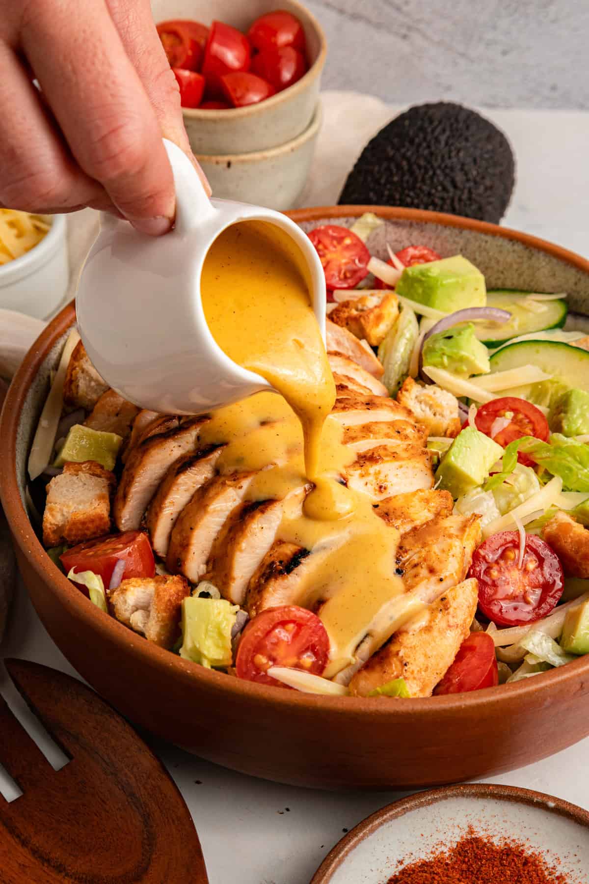 Grilled chicken sits atop a bed of lettuce with cucumber, avocado, tomato, and sharp cheddar cheese in this Honey Mustard Chicken Salad. Pouring honey mustard dressing over a salad in a bowl