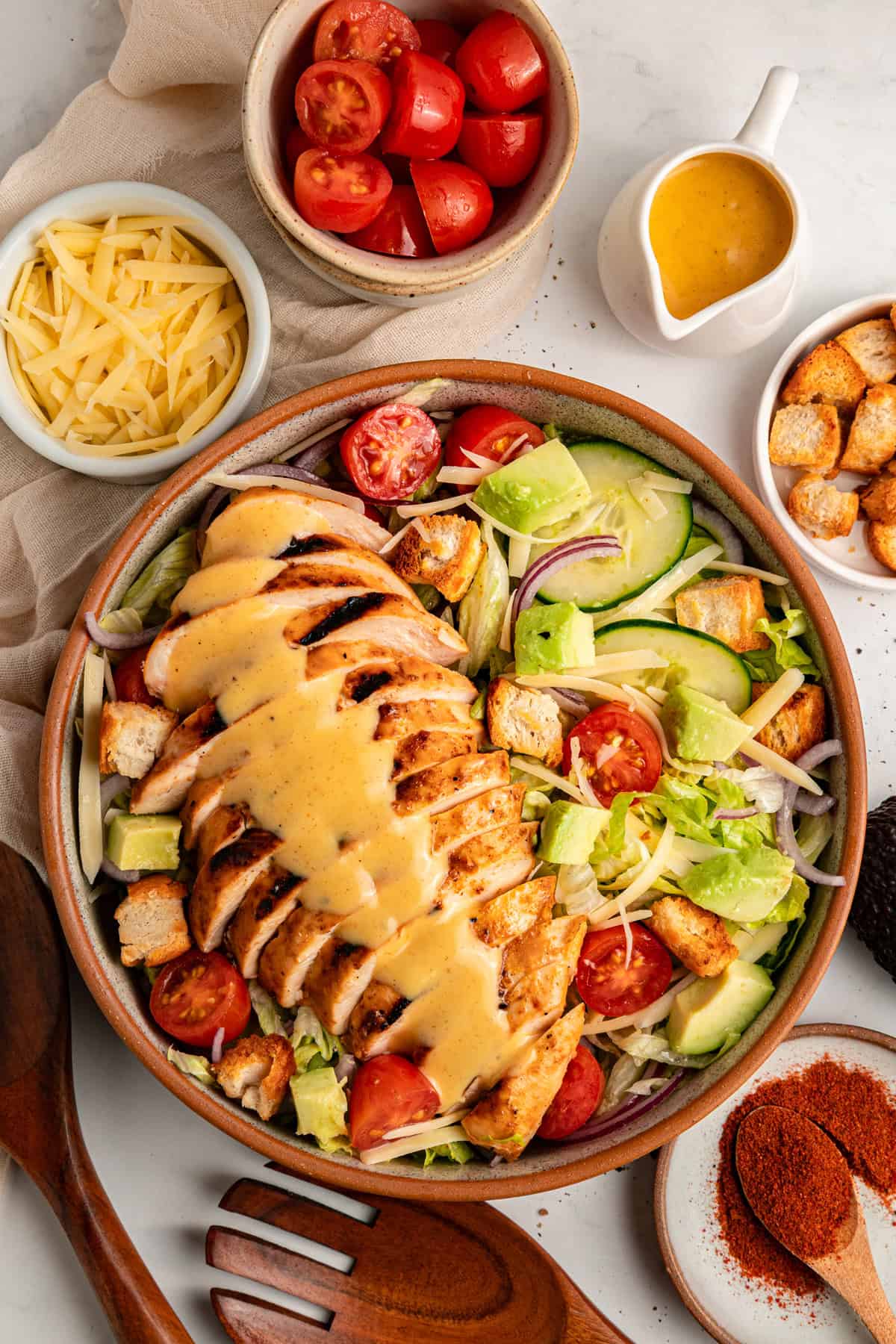 Grilled chicken sits atop a bed of lettuce with cucumber, avocado, tomato, and sharp cheddar cheese in this Honey Mustard Chicken Salad. Overhead view of honey mustard chicken salad in a wooden bowl