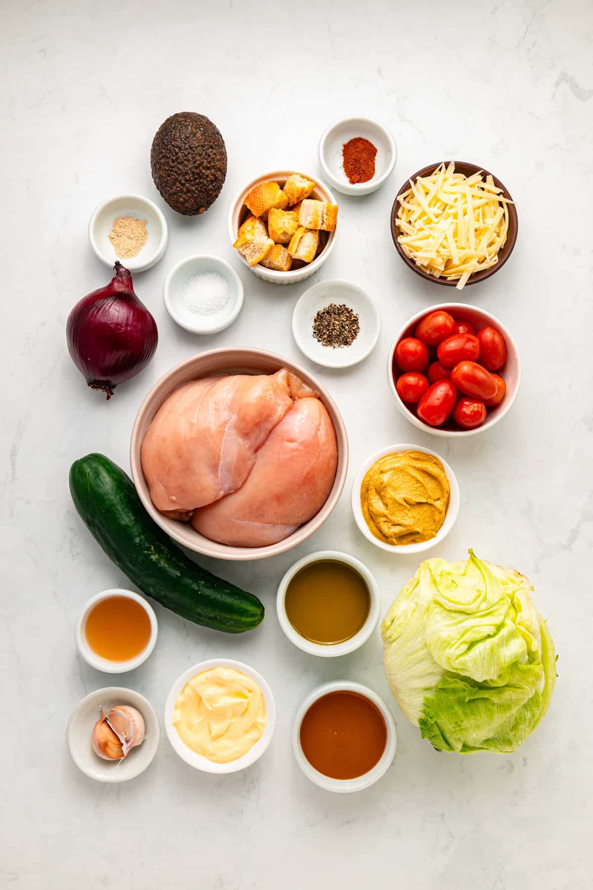 Grilled chicken sits atop a bed of lettuce with cucumber, avocado, tomato, and sharp cheddar cheese in this Honey Mustard Chicken Salad. Overhead view of ingredients needed to make honey mustard chicken salad