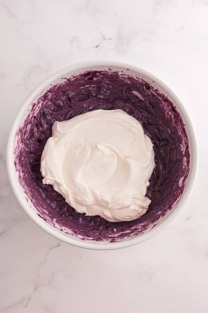 Moist lemon cakes, tangy blueberry cheesecake filling, & tart lemon frosting make up the layers of this Lemon Blueberry Cheesecake Cake. Whipped cream added to blueberry cheesecake filling