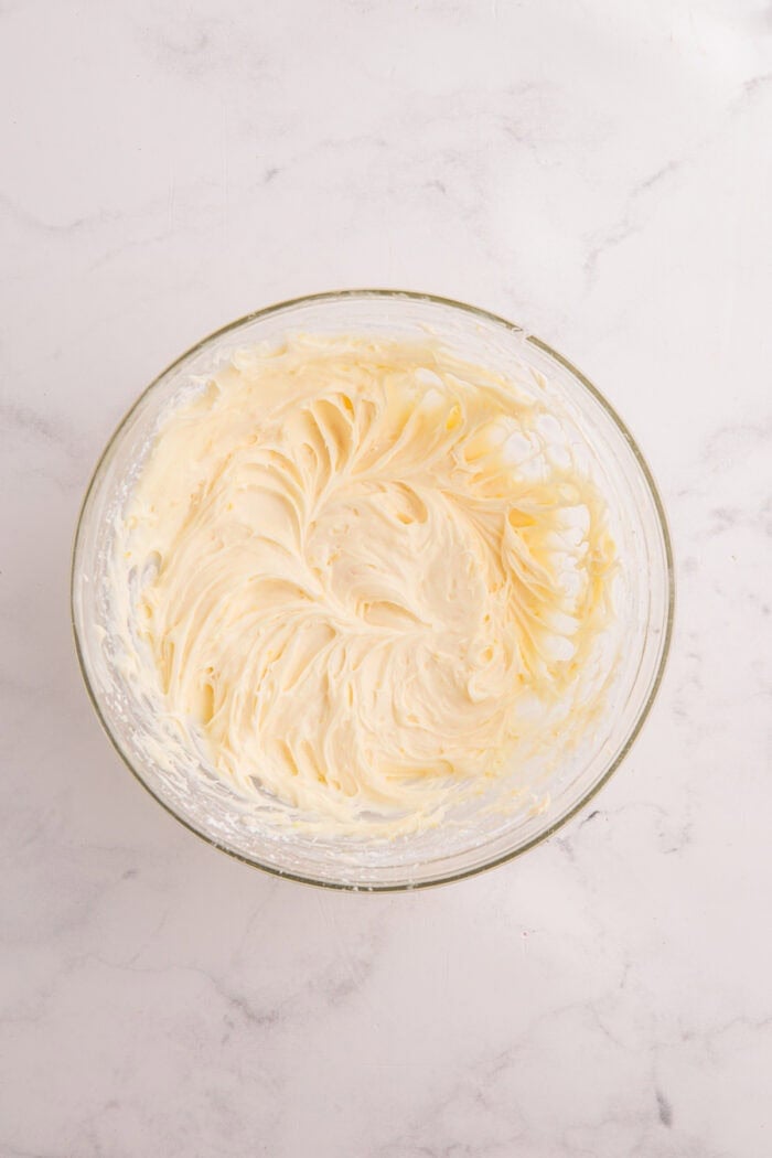 Moist lemon cakes, tangy blueberry cheesecake filling, & tart lemon frosting make up the layers of this Lemon Blueberry Cheesecake Cake. Lemon cream cheese frosting in a bowl