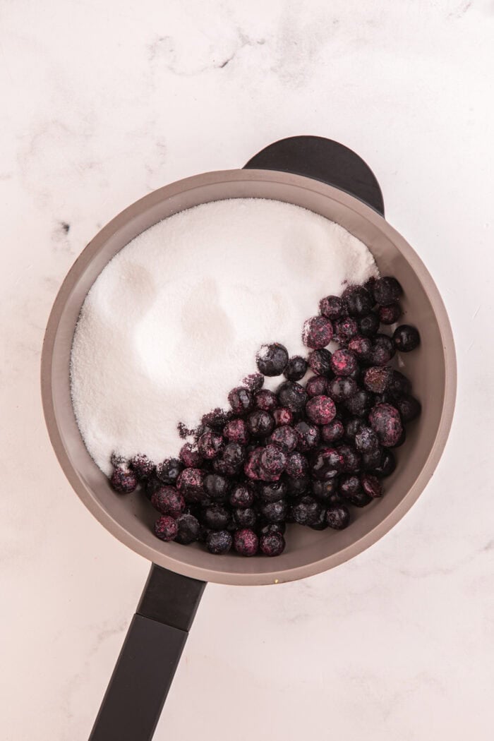 Moist lemon cakes, tangy blueberry cheesecake filling, & tart lemon frosting make up the layers of this Lemon Blueberry Cheesecake Cake. Sugar and blueberries in a pan