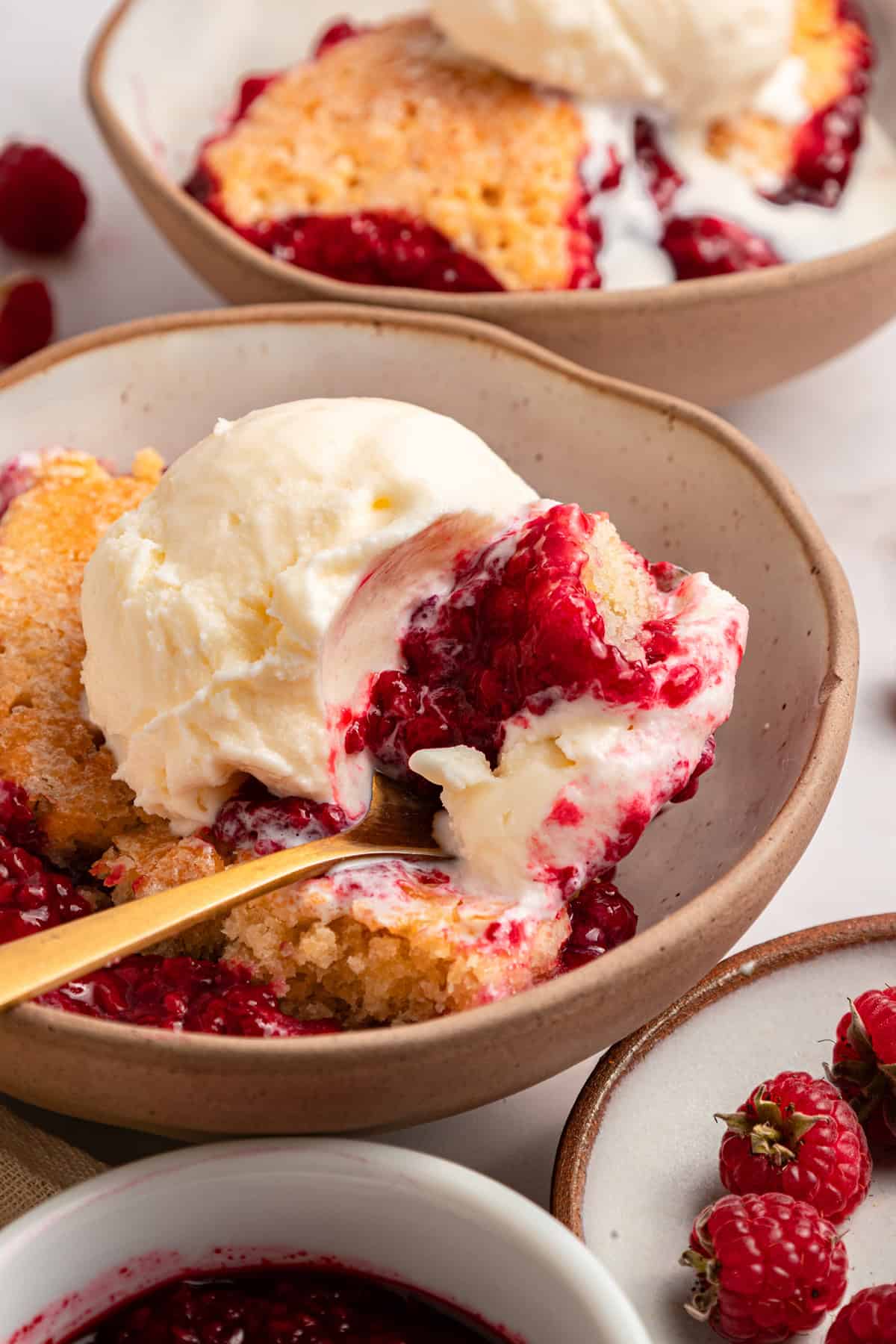 This rustic Raspberry Cobbler recipe is made with a jammy fruit filling and a golden, biscuit-style topping. Quick & easy! A spoonful of raspberry cobbler with vanilla ice cream over a bowl