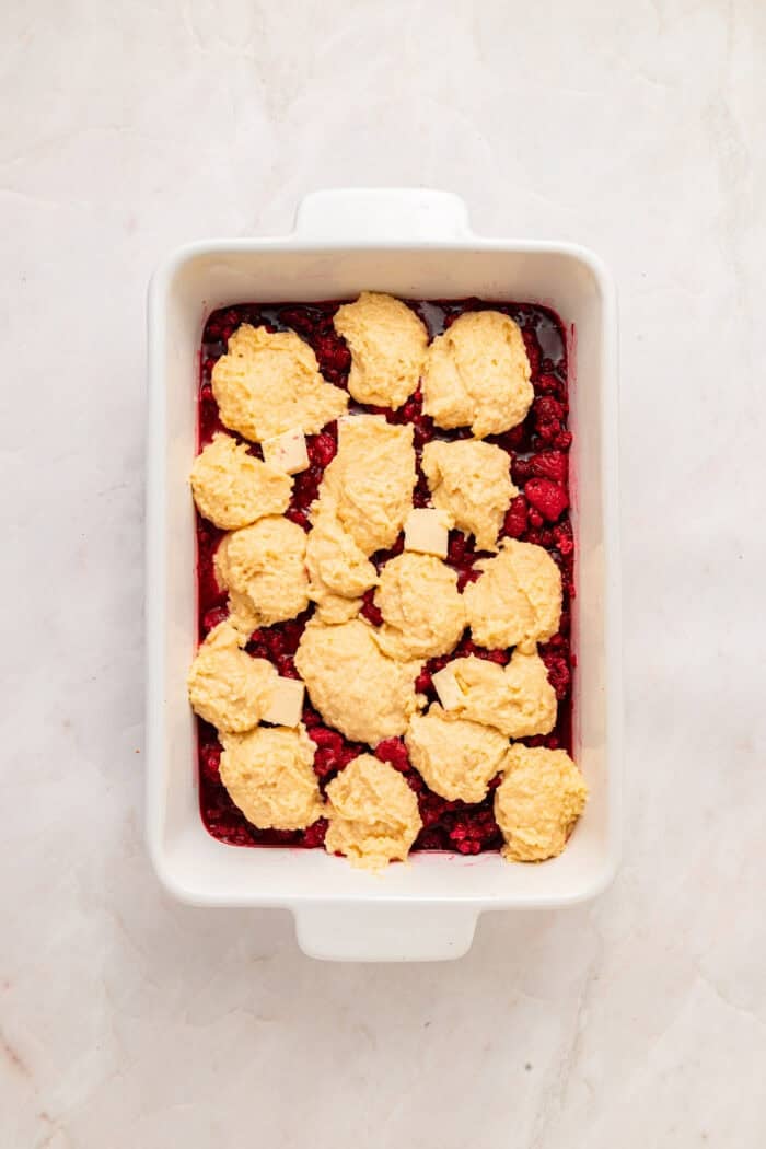 Spoonfuls of cobbler topping on top of raspberry filling