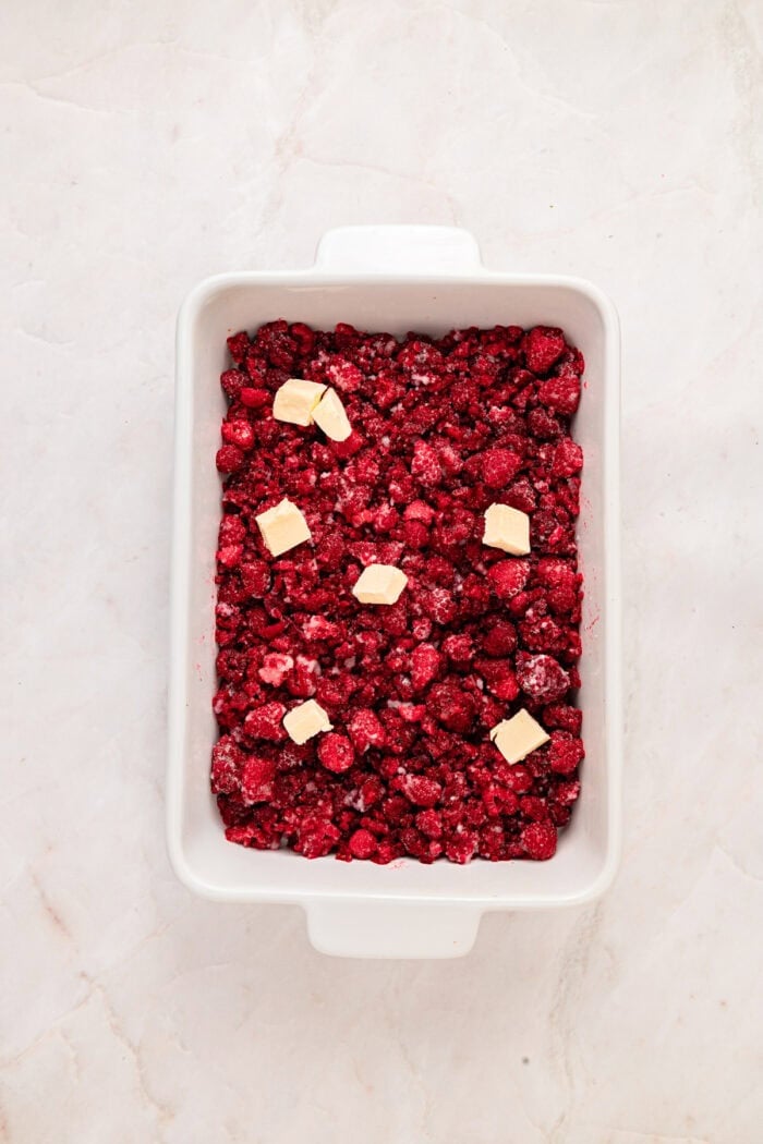 This rustic Raspberry Cobbler recipe is made with a jammy fruit filling and a golden, biscuit-style topping. Quick & easy! Raspberry filling in a baking dish topped with butter