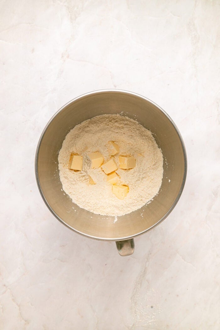 This rustic Raspberry Cobbler recipe is made with a jammy fruit filling and a golden, biscuit-style topping. Quick & easy! Cubed butter added to a bowl with flour