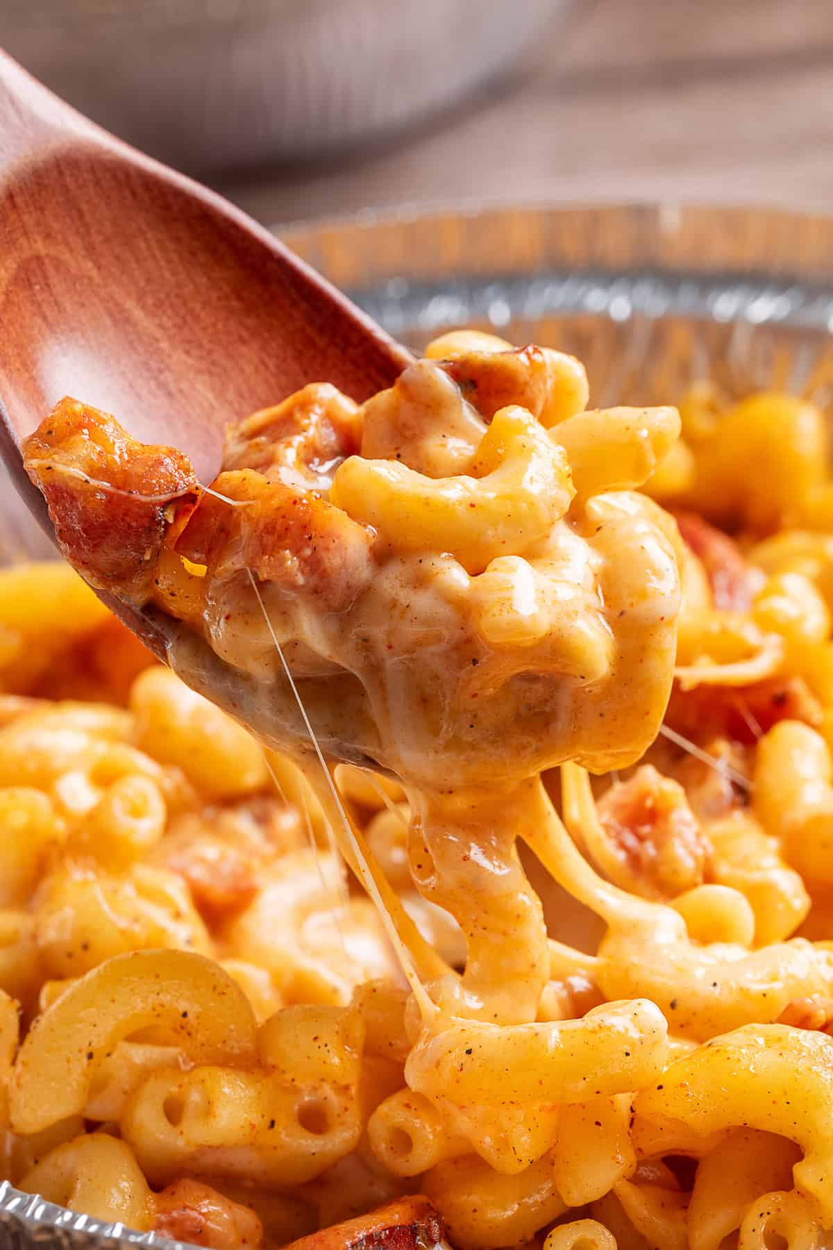 Close up of a wooden spoon serving sausage mac and cheese