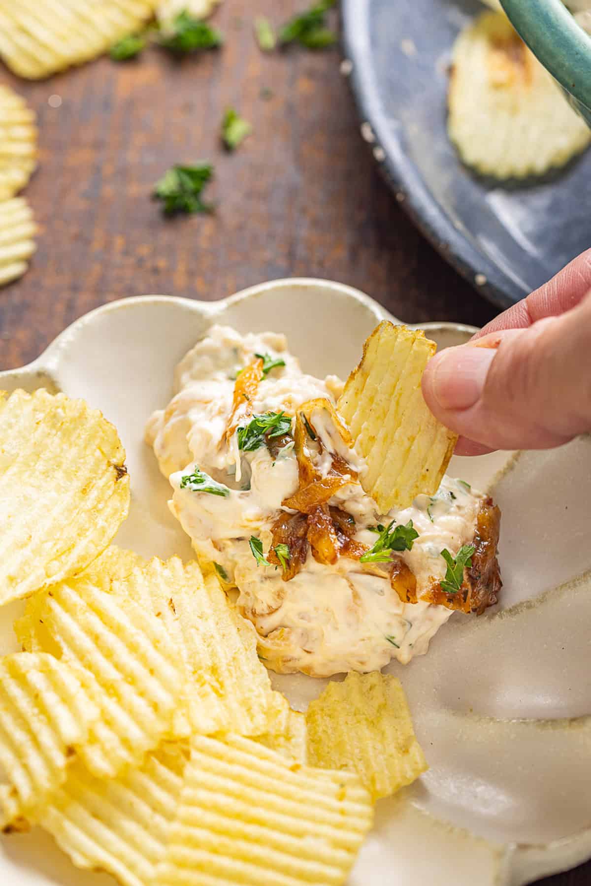 Sweet, savory caramelized onions are combined with tangy sour cream and cream cheese, plus a few seasonings, to make Caramelized Onion Dip. A plate with chips and caramelized onion dip
