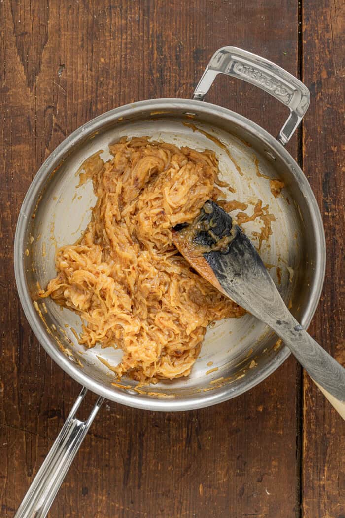 Sweet, savory caramelized onions are combined with tangy sour cream and cream cheese, plus a few seasonings, to make Caramelized Onion Dip. A spatula stirring caramelized onions in a pan
