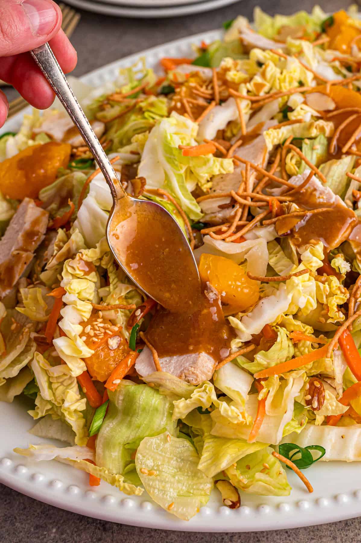 Grilled chicken, crunchy veggies, and mandarin oranges are tossed in a ginger sesame dressing in this easy Chinese Chicken Salad recipe. Spooning dressing over Chinese chicken salad
