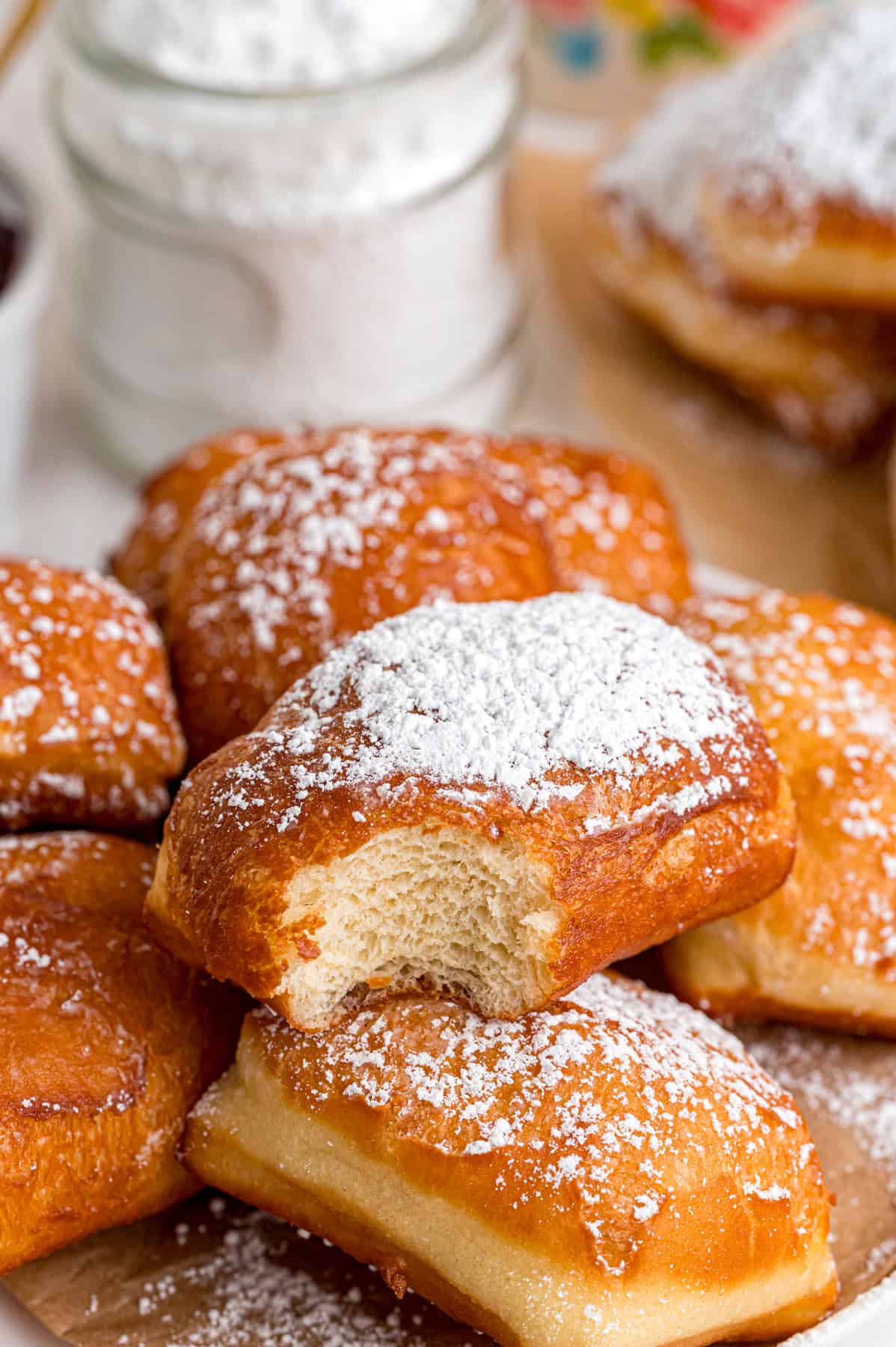 This Beignets recipe is an easy homemade version of the popular New Orleans fried square donuts. Soft & fluffy! A plate of beignets, one with a bite missing