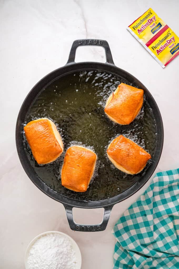 This Beignets recipe is an easy homemade version of the popular New Orleans fried square donuts. Soft & fluffy! Beignets frying in a pan