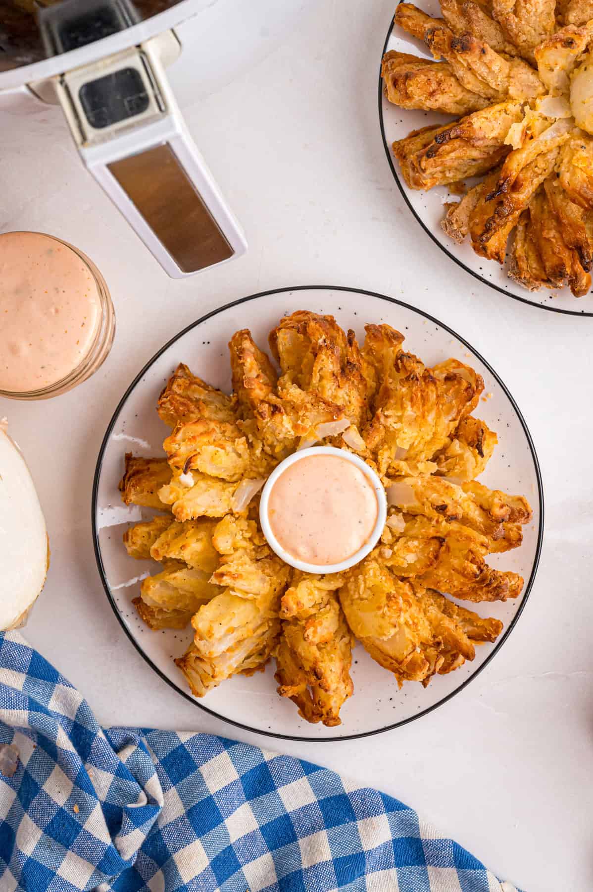 Onions are coated in a seasoned batter, then deep-fried to crispy, golden perfection in this Blooming Onion recipe. Overhead view of a blooming onion on a plate with sauce