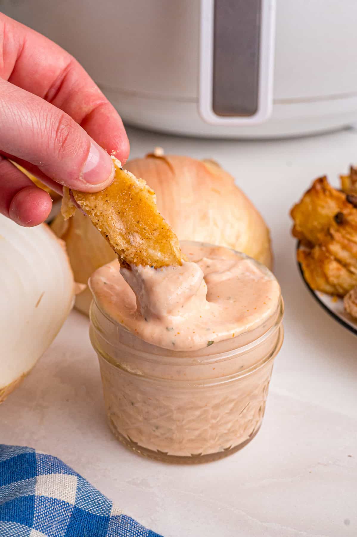This copycat Outback Steakhouse Blooming Onion Sauce is creamy, tangy, and spicy, and ready in just 5 minutes. A hand dipping an onion petal in a jar of blooming onion dipping sauce