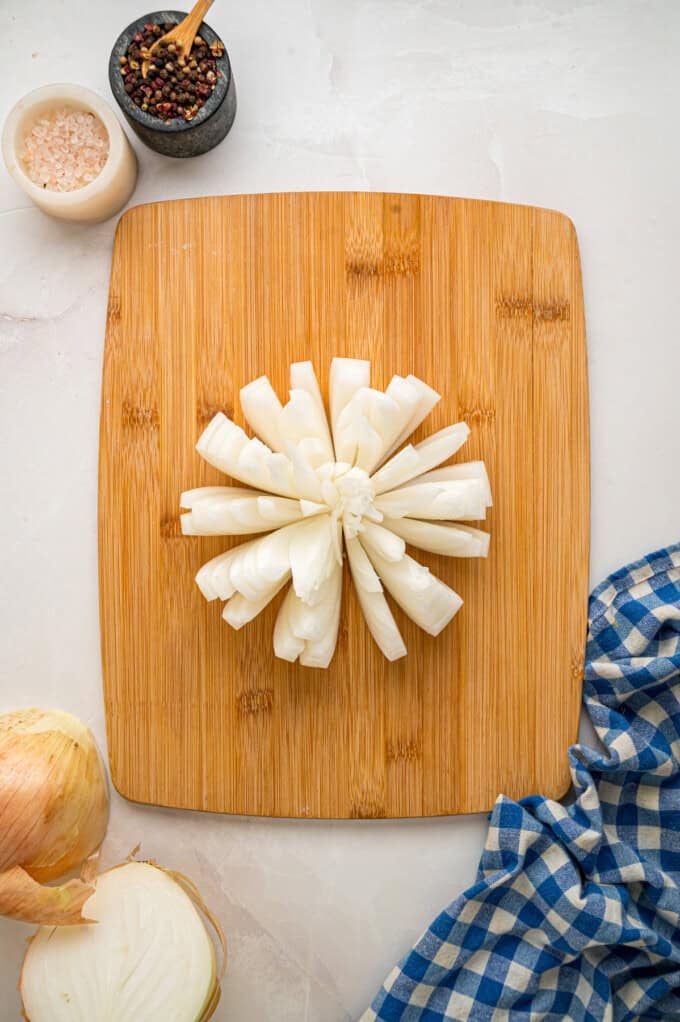 Onions are coated in a seasoned batter, then deep-fried to crispy, golden perfection in this Blooming Onion recipe. An onion sliced to make a blooming onion on a cutting board
