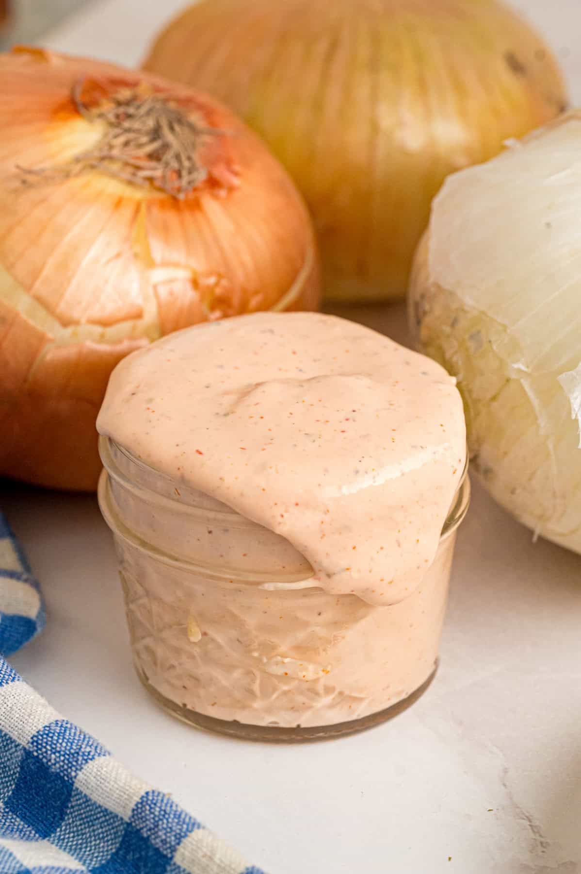 This copycat Outback Steakhouse Blooming Onion Sauce is creamy, tangy, and spicy, and ready in just 5 minutes. A small glass jar of blooming onion sauce in front of onions