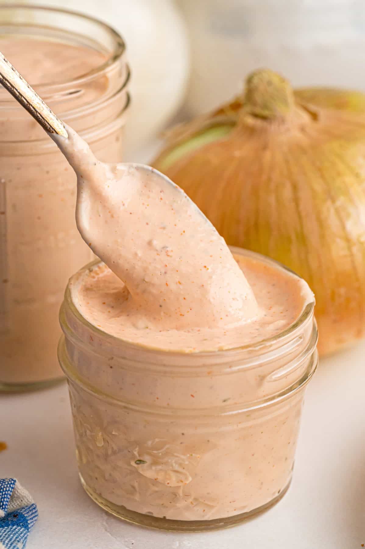 This copycat Outback Steakhouse Blooming Onion Sauce is creamy, tangy, and spicy, and ready in just 5 minutes. A spoon above a jar of blooming onion dipping sauce