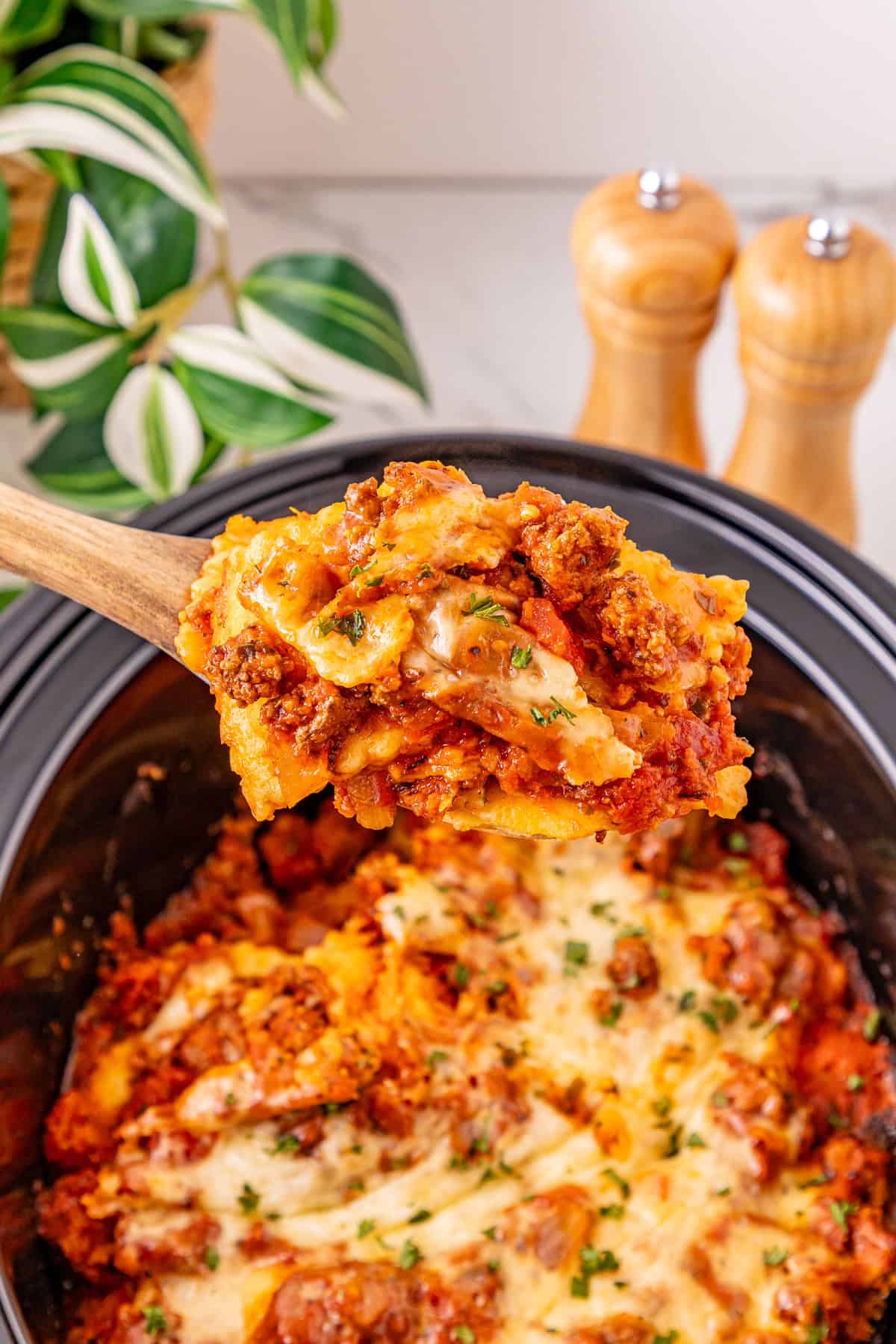 Ground beef with pasta sauce, frozen ravioli, and shredded cheese are layered to make this Crockpot Ravioli Lasagna. A spoon serving crockpot ravioli lasagna