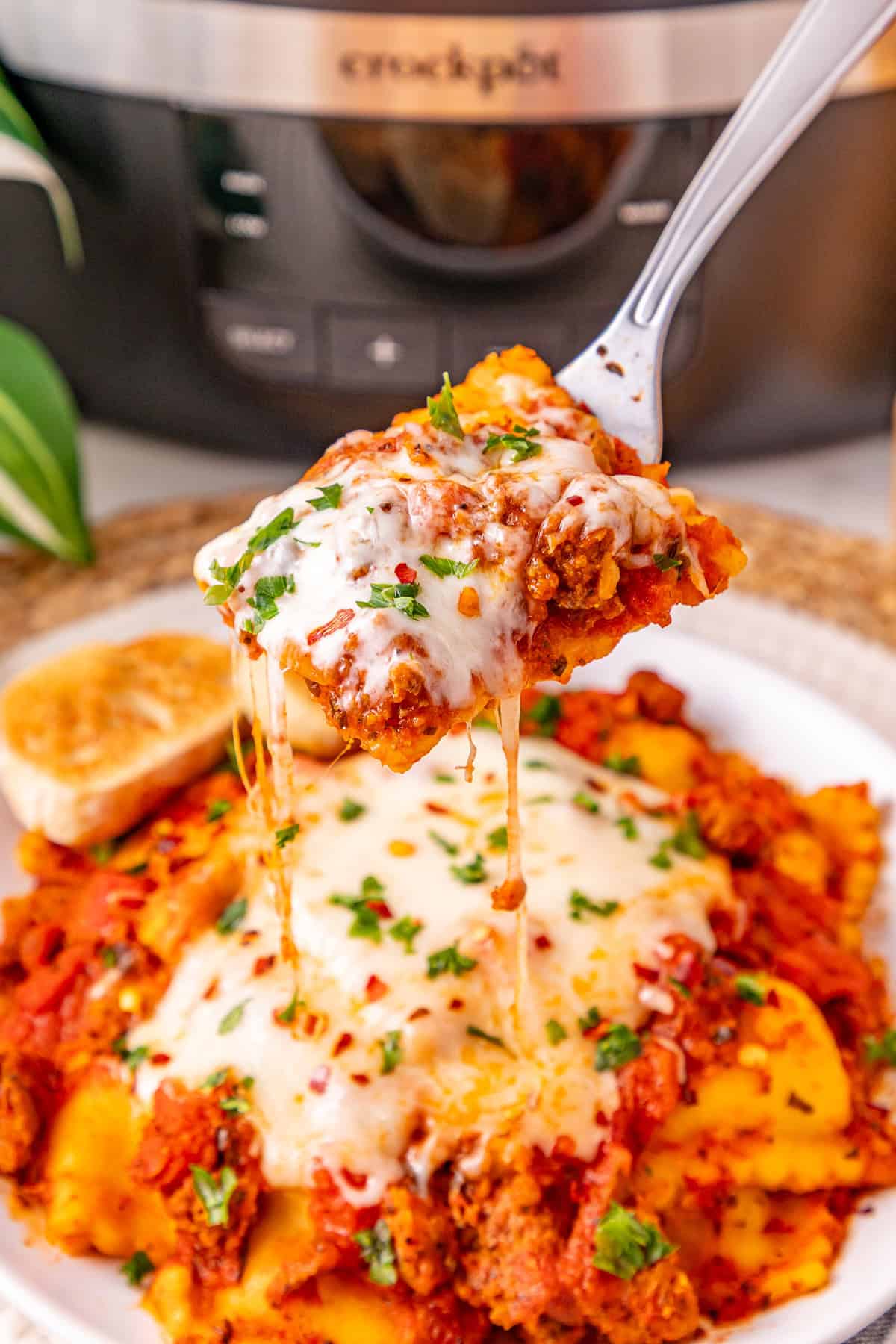 Ground beef with pasta sauce, frozen ravioli, and shredded cheese are layered to make this Crockpot Ravioli Lasagna. A bite of crockpot ravioli lasagna over a plate