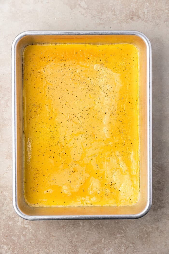 Made with English muffins, sheet pan eggs, cheese, and meat, these Make Ahead Breakfast Sandwiches are perfect for busy mornings! Overhead view of sheet pan eggs sprinkled with pepper