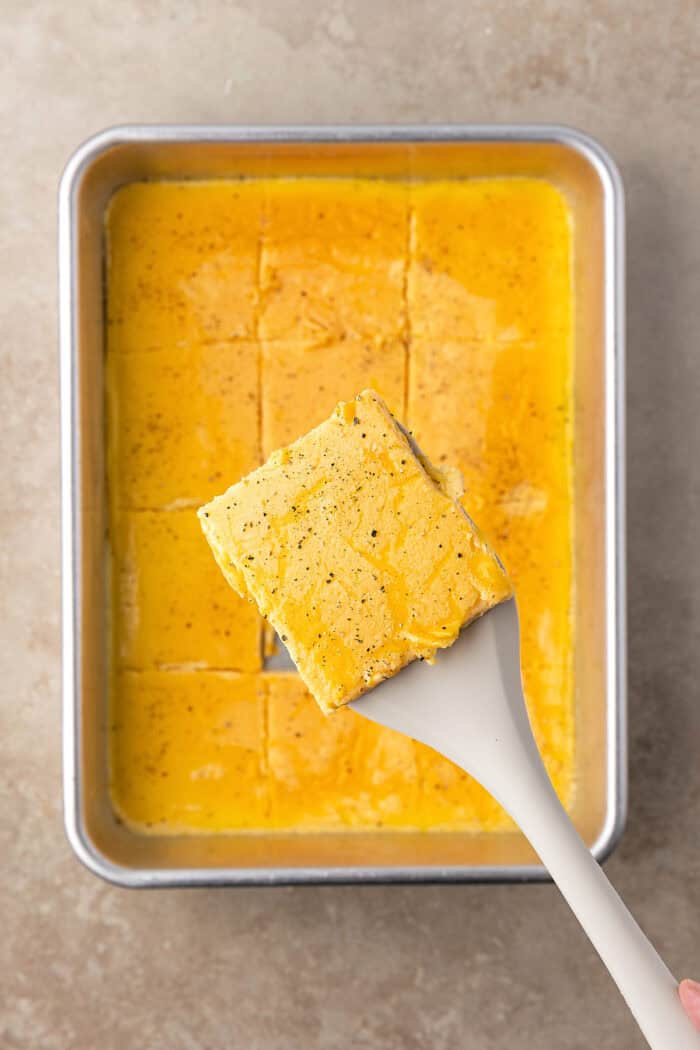 Made with English muffins, sheet pan eggs, cheese, and meat, these Make Ahead Breakfast Sandwiches are perfect for busy mornings! A square of sheet pan eggs on a spatula above the pan