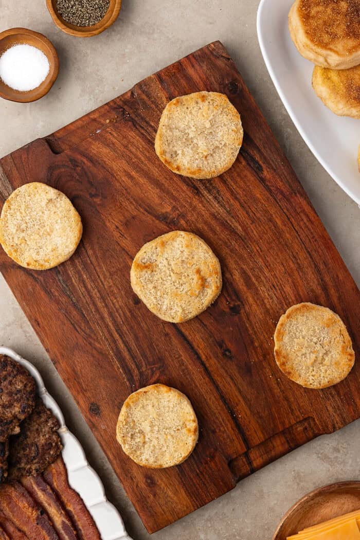 Made with English muffins, sheet pan eggs, cheese, and meat, these Make Ahead Breakfast Sandwiches are perfect for busy mornings! Toasted sourdough English muffin halves on a cutting board