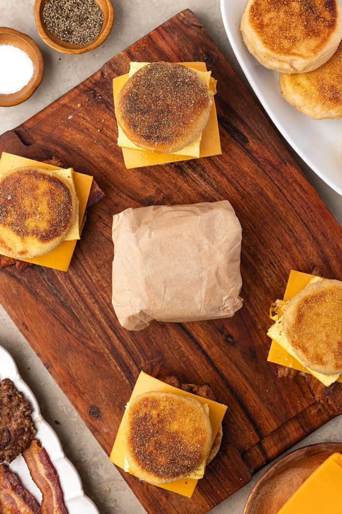 Made with English muffins, sheet pan eggs, cheese, and meat, these Make Ahead Breakfast Sandwiches are perfect for busy mornings! English muffins sandwiches on a cutting board, one wrapped in parchment paper