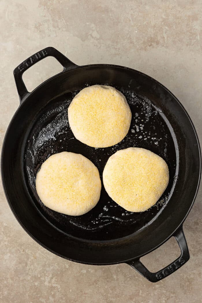 These Sourdough English Muffins are soft, chewy, and full of the classic nooks and crannies everyone loves. Sourdough English muffins cooking in a cast iron skillet