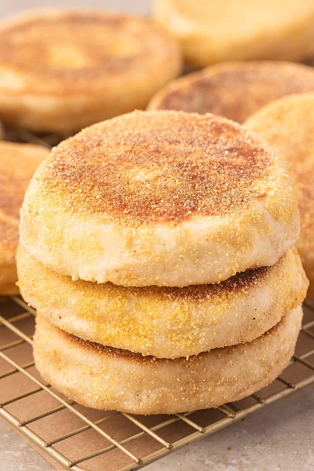 These Sourdough English Muffins are soft, chewy, and full of the classic nooks and crannies everyone loves. Sourdough English muffins stacked on a cooling rack