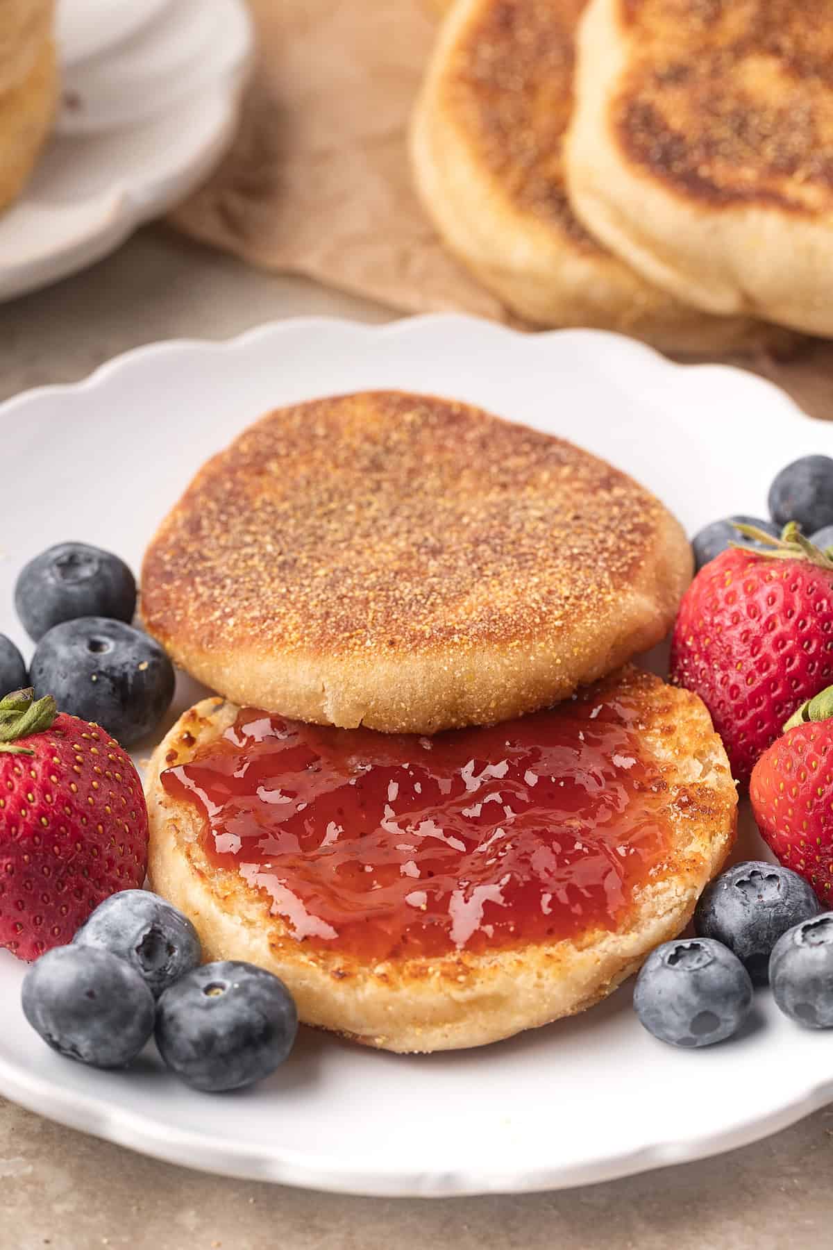 These Sourdough English Muffins are soft, chewy, and full of the classic nooks and crannies everyone loves. A sourdough English muffin with jam on a plate with fresh fruit