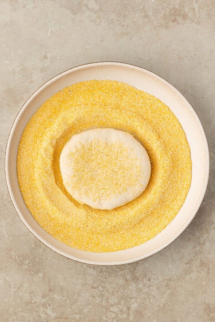 These Sourdough English Muffins are soft, chewy, and full of the classic nooks and crannies everyone loves. Dough pressed into a plate of cornmeal