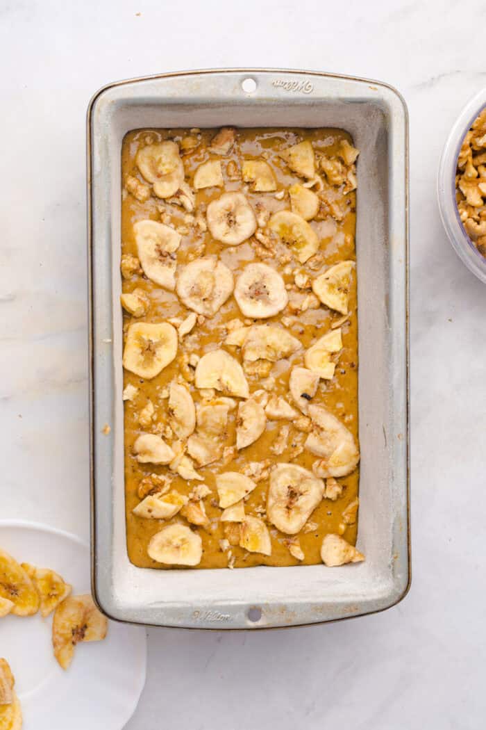 This copycat Starbucks Banana Bread is soft and moist, with lots of sweet banana flavor and warm spices. One bowl + 15 minutes! Chopped walnuts and banana chips on top of banana bread batter in a loaf pan