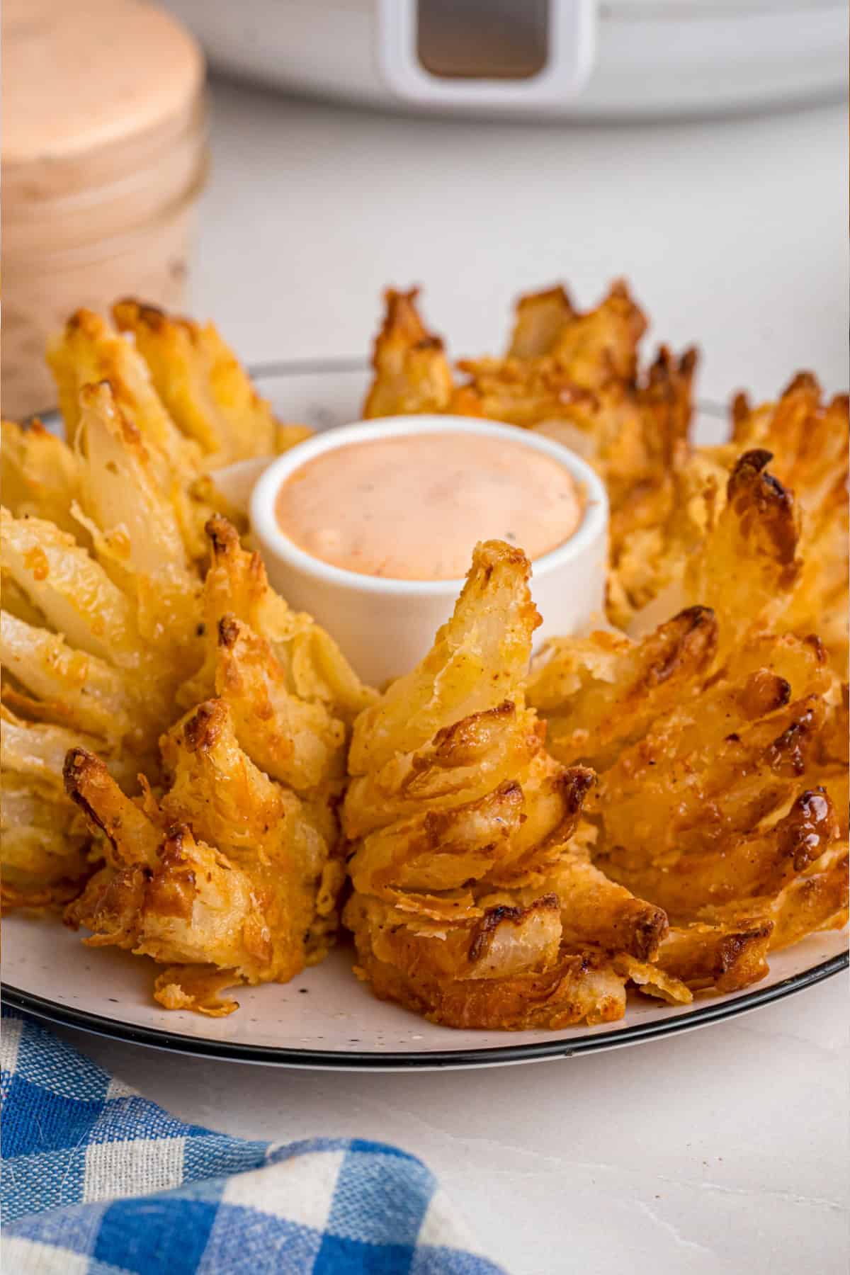Onions are coated in a seasoned batter, then deep-fried to crispy, golden perfection in this Blooming Onion recipe. Blooming Onion on a plate with blooming onion sauce in the center