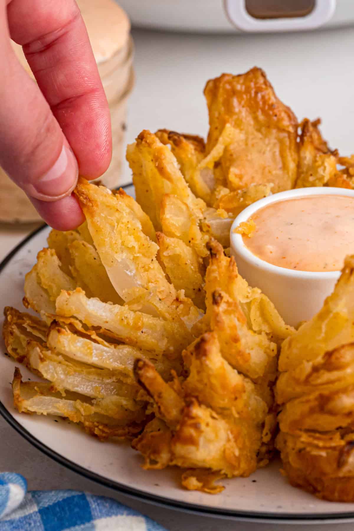 Onions are coated in a seasoned batter, then deep-fried to crispy, golden perfection in this Blooming Onion recipe. Hand pulling off a piece of blooming onion
