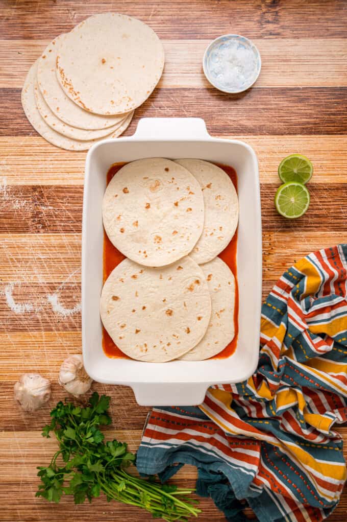With layers of tortillas, enchilada sauce, gooey cheese, and chicken and beans, Chicken Enchilada Casserole is an easy weeknight dinner. Tortillas on top of enchilada sauce in a casserole dish