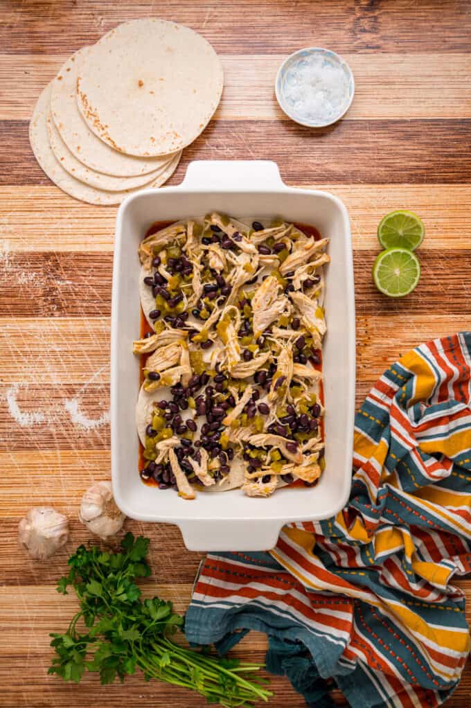 With layers of tortillas, enchilada sauce, gooey cheese, and chicken and beans, Chicken Enchilada Casserole is an easy weeknight dinner. Chicken filling on top of the tortillas