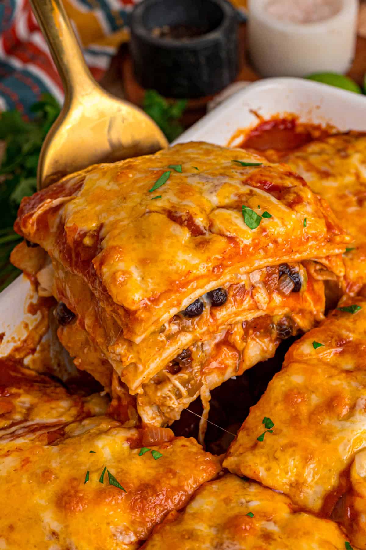 A slice of Chicken Enchilada Casserole being lifted out of the pan with a spatula.
