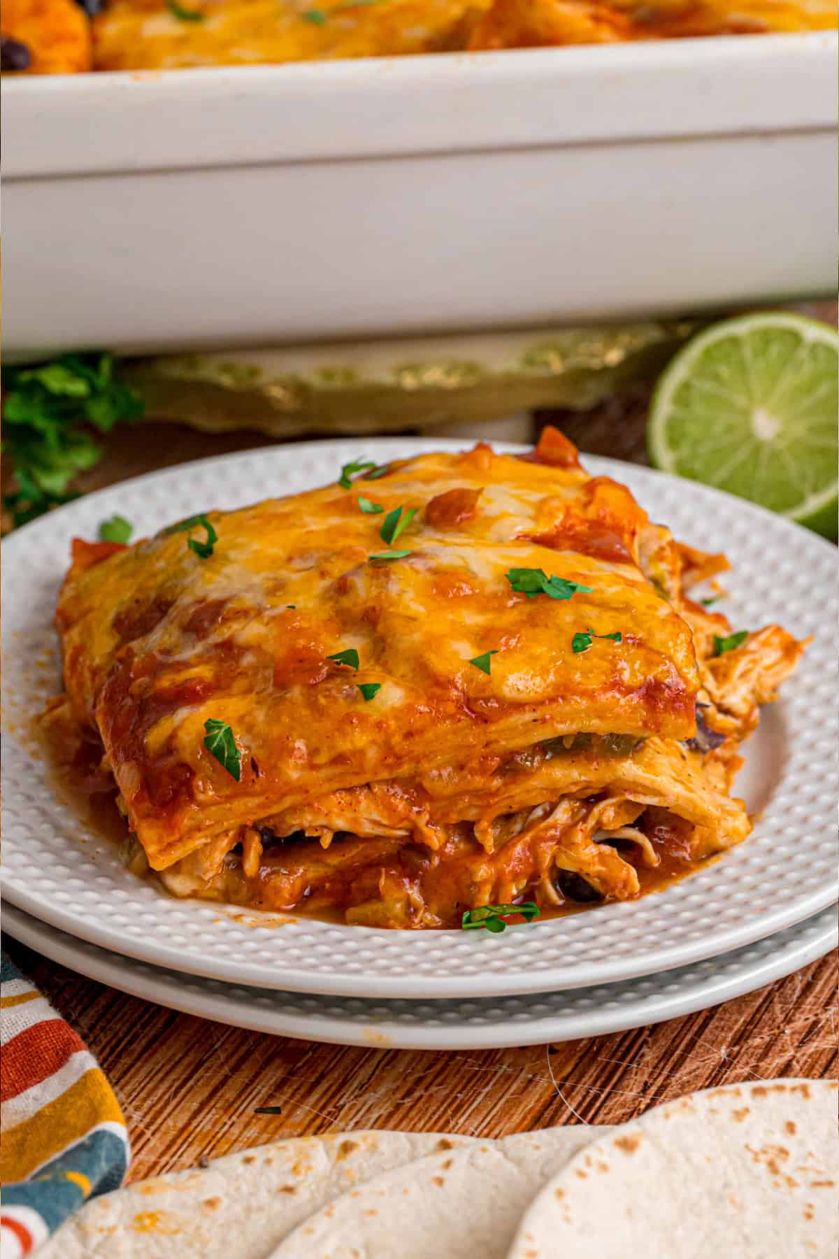 With layers of tortillas, enchilada sauce, gooey cheese, and chicken and beans, Chicken Enchilada Casserole is an easy weeknight dinner. a slice of chicken enchilada casserole on a plate