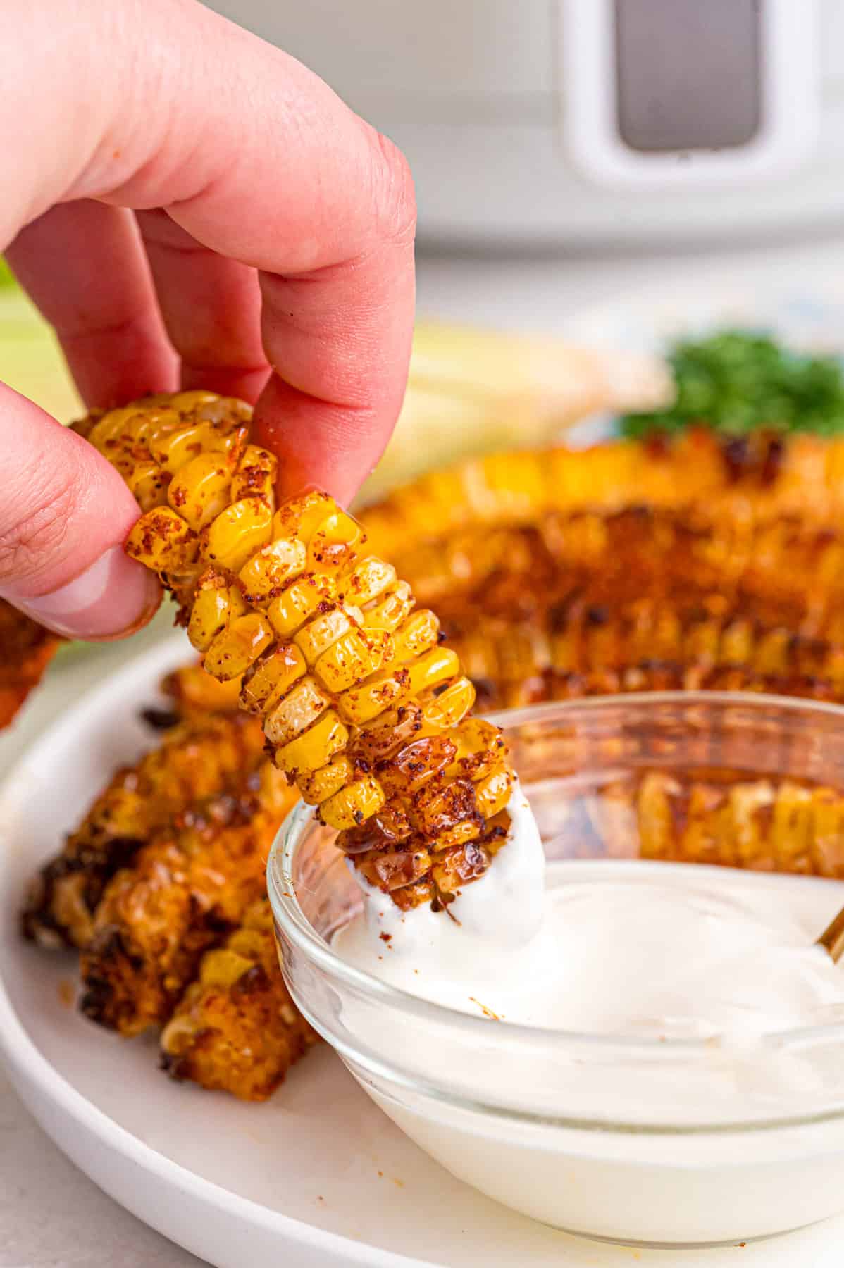 These easy Corn Ribs are coated in warm, smoky spices, cooked in the air fryer or grill, drizzled with lime crema. A hand dipping a corn rib into lime crema