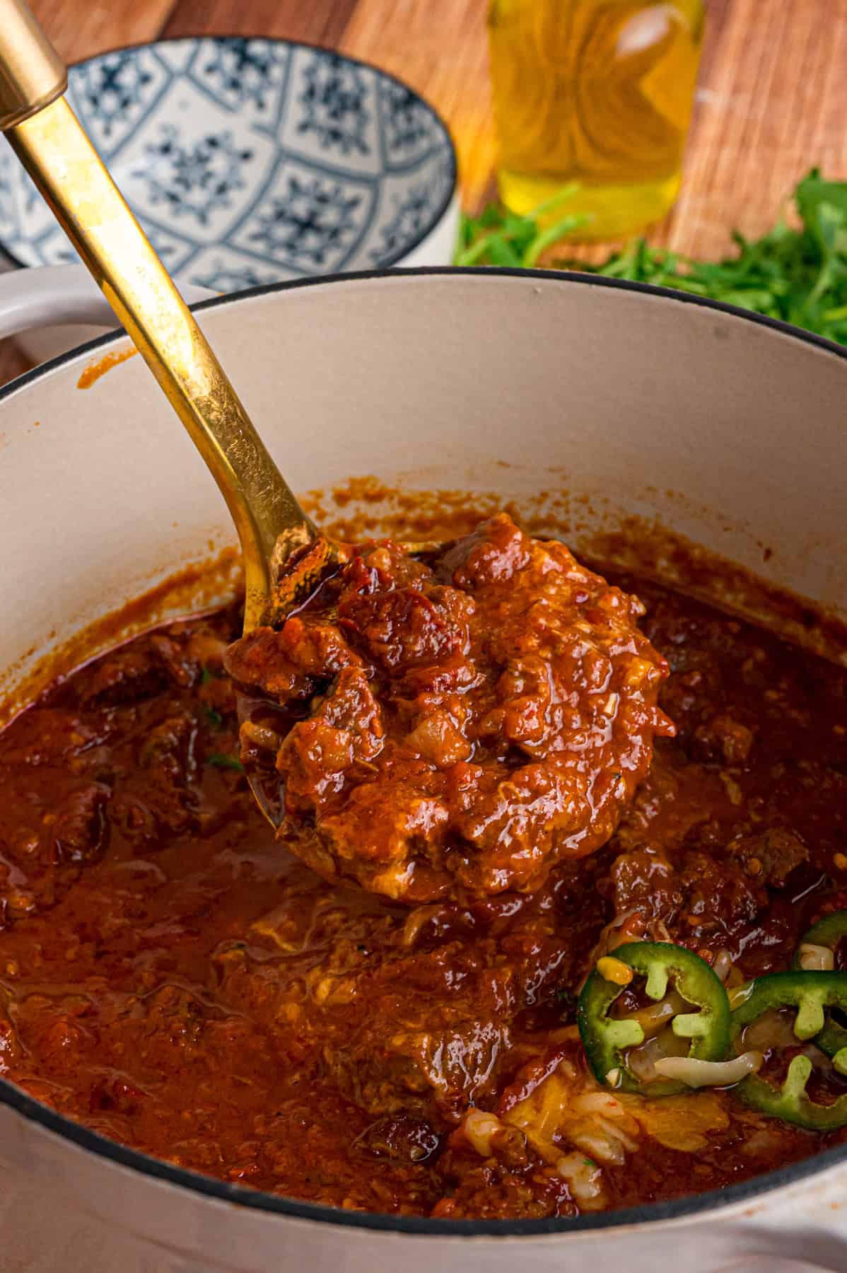 Seared chunks of chuck roast are simmered with crushed tomatoes, jalapenos, and chipotles in adobo sauce to make this Texas Chili recipe. A ladle of Texas chili above the pot