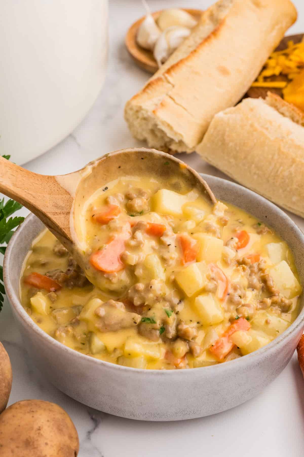 A wooden spoon serving sausage potato soup into a bowl