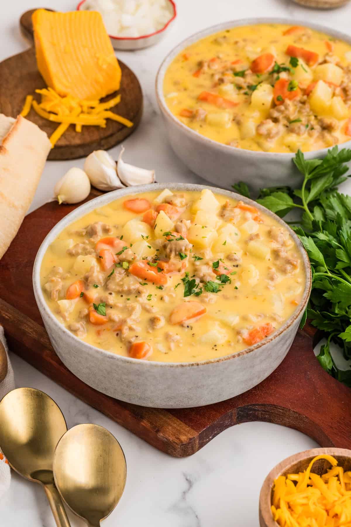 This Sausage Potato Soup is rich, creamy, and loaded with savory Italian sausage, tender potatoes, sweet carrots, and sharp cheddar cheese. A heaping bowl of sausage potato soup on a cutting board