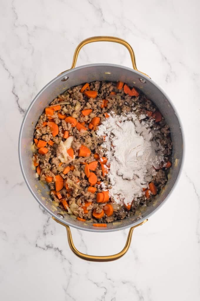 This Sausage Potato Soup is rich, creamy, and loaded with savory Italian sausage, tender potatoes, sweet carrots, and sharp cheddar cheese. Flour added to cooked sausage and carrots in a pot