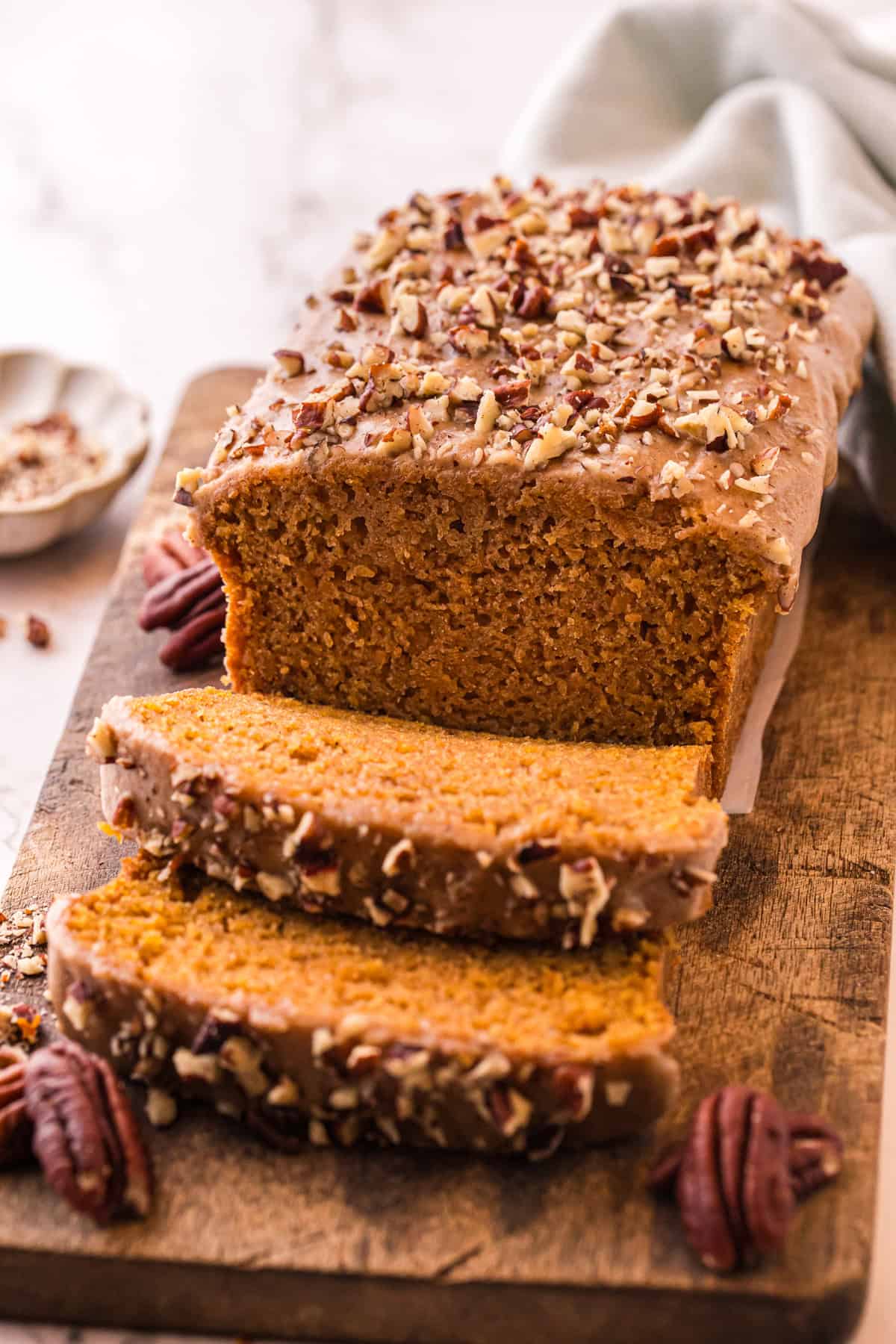 This Sweet Potato Bread is moist, dense, and packed with warm spices. Topped with butter glaze and pecans! Perfect for fall. A loaf of sweet potato bread with a few pieces sliced