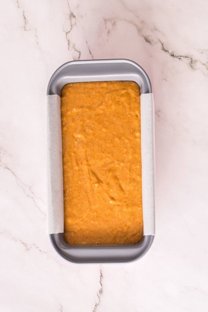 This Sweet Potato Bread is moist, dense, and packed with warm spices. Topped with butter glaze and pecans! Perfect for fall. Sweet potato bread batter in a loaf pan